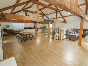 Un loft espacioso con vigas de madera expuestas, un comedor con mesa y bancos de madera, una cocina con armarios blancos y una sala de estar con sofá y cojines.
