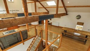 A spacious loft with wooden beams, a staircase, and a dining area. - Upper House Barn (Oldham)
