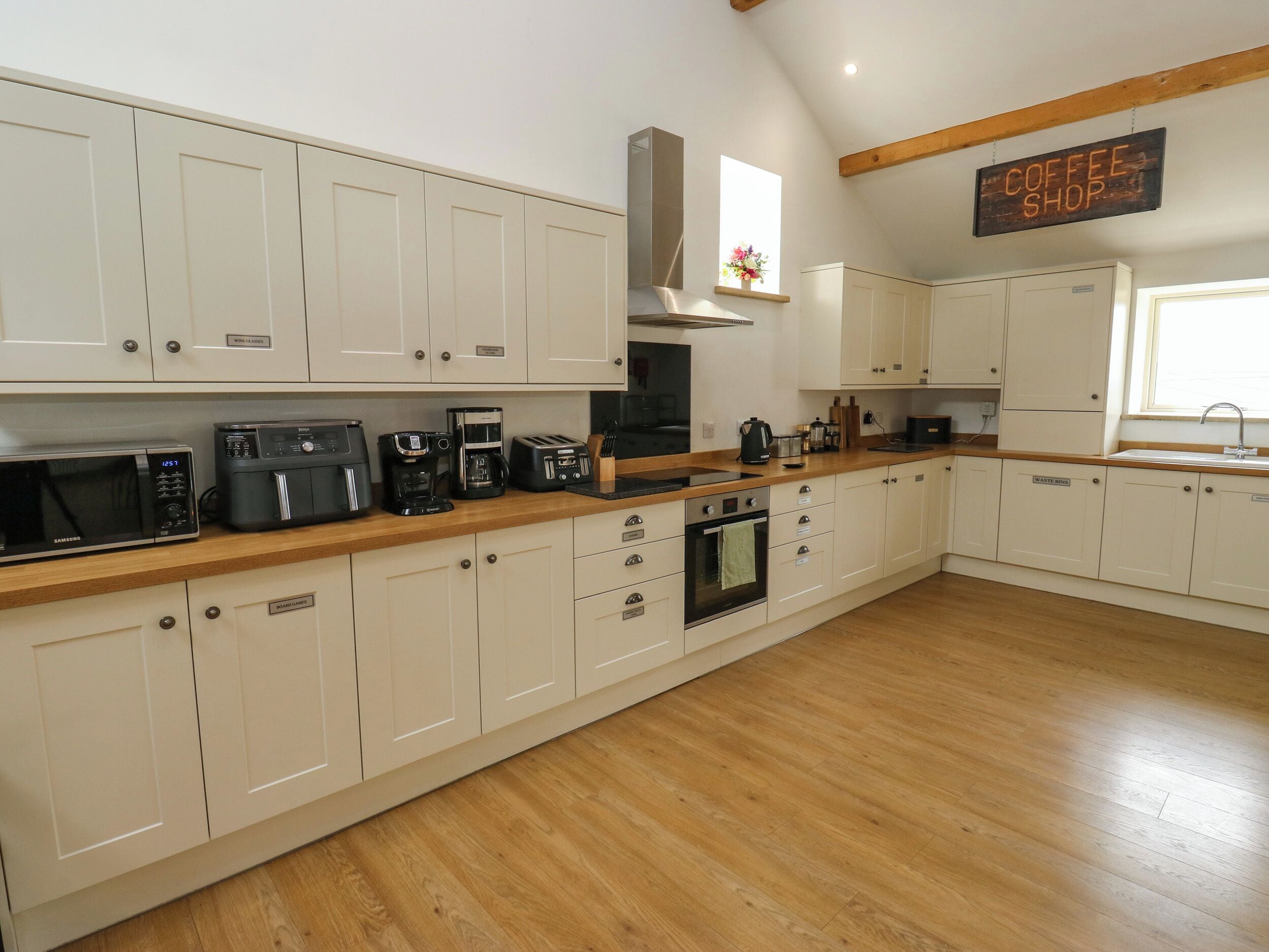 A kitchen with white cabinets, a wooden countertop, a coffee machine, and a sign indicating a coffee shop.