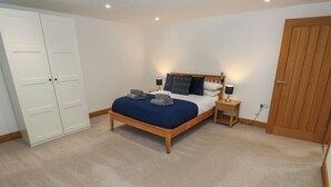 A bedroom with a bed, bedside tables, a wardrobe, and a door. - Upper House Barn (Oldham)