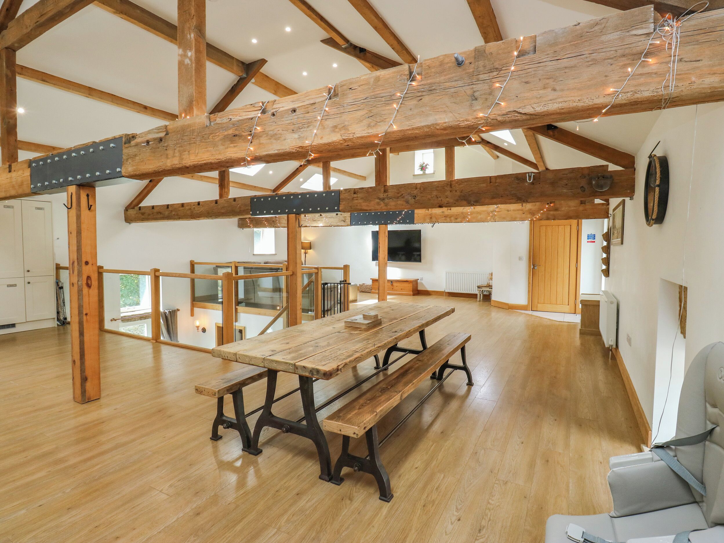 A spacious room with a wooden table and benches, high ceilings with exposed beams, and a large window providing natural light.