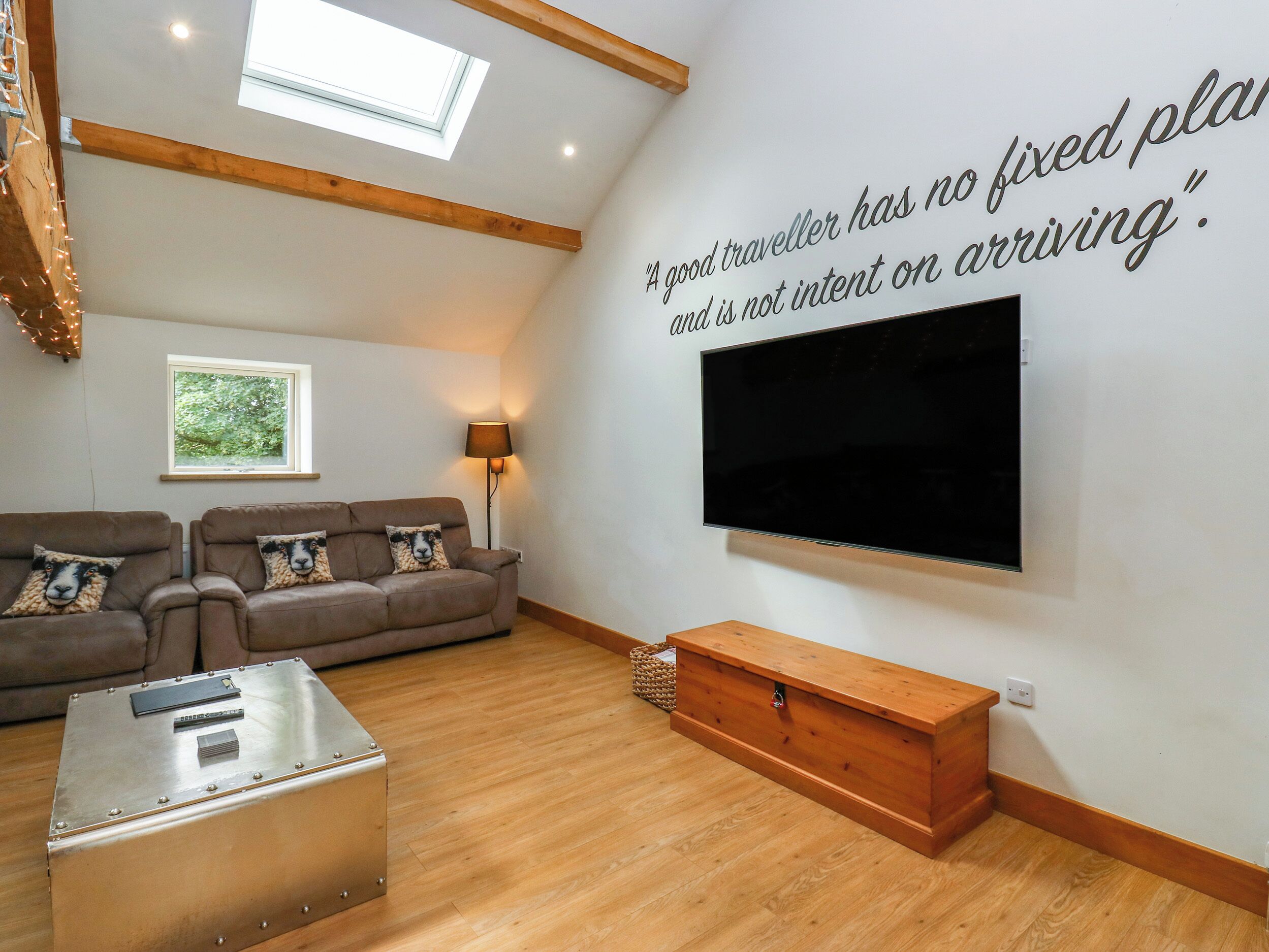 Una sala de estar con sofá, televisor de pantalla plana, mueble de madera y techo con tragaluces.