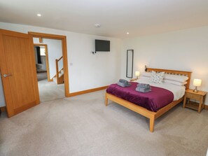A bedroom with a wooden bed, a television on the wall, and a carpeted floor.