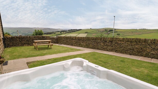 Un bain à remous dans un jardin, avec un mur en pierre, une table de pique-nique et une vue sur des collines ondoyantes.