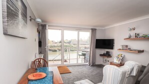 A living room with a dining table, chairs, a striped armchair, a sofa, a TV, and a view of a water body through a sliding door. - 3 Tidal (Rye)