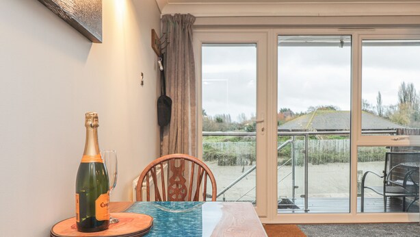 A dining area with a table, chairs, a bottle of champagne, and a view through a glass door. - 3 Tidal (Rye)
