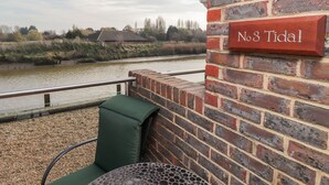 A brick wall with a sign reading "No 3 Tidal" and a green chair by a railing overlooking a river. - 3 Tidal (Rye)