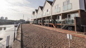A row of modern, two-story residential buildings with balconies, situated next to a calm body of water. - 3 Tidal (Rye)