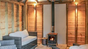 A cozy room with wicker furniture, a wood-burning stove, and wooden walls. - Hillside Lodge (Ludlow)