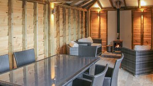 A cozy wooden cabin with a glass dining table, wicker chairs, a sofa, and a wood-burning stove. - Hillside Lodge (Ludlow)