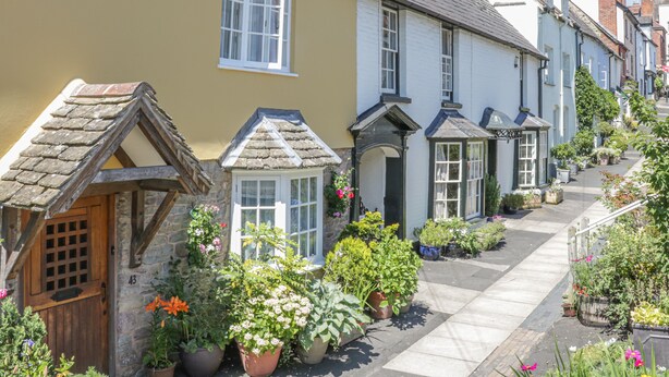 A row of traditional houses with stone foundations and pitched roofs, a narrow street with potted plants, and a clear blue sky. - Hillside Lodge (Ludlow)