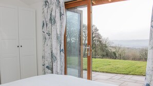 A bedroom with a large bed, a sliding glass door leading to a patio with a grassy area and trees. - Hillside Lodge (Ludlow)