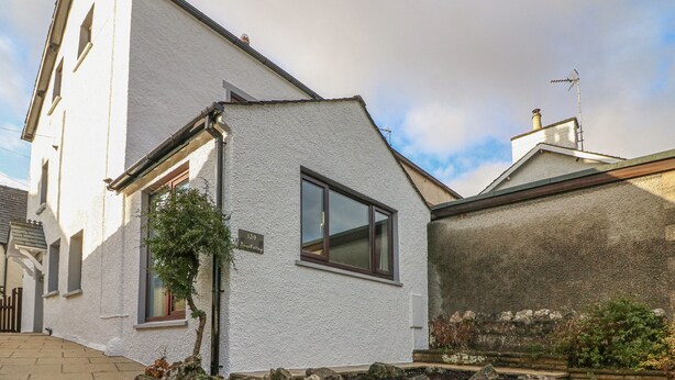 A white building with a small garden area, a visible number '129', and a chimney. - Rose Cottage (Grange-over-Sands)