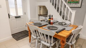 A dining area with a wooden table set for four, white chairs, and a staircase in the background. - Rose Cottage (Grange-over-Sands)