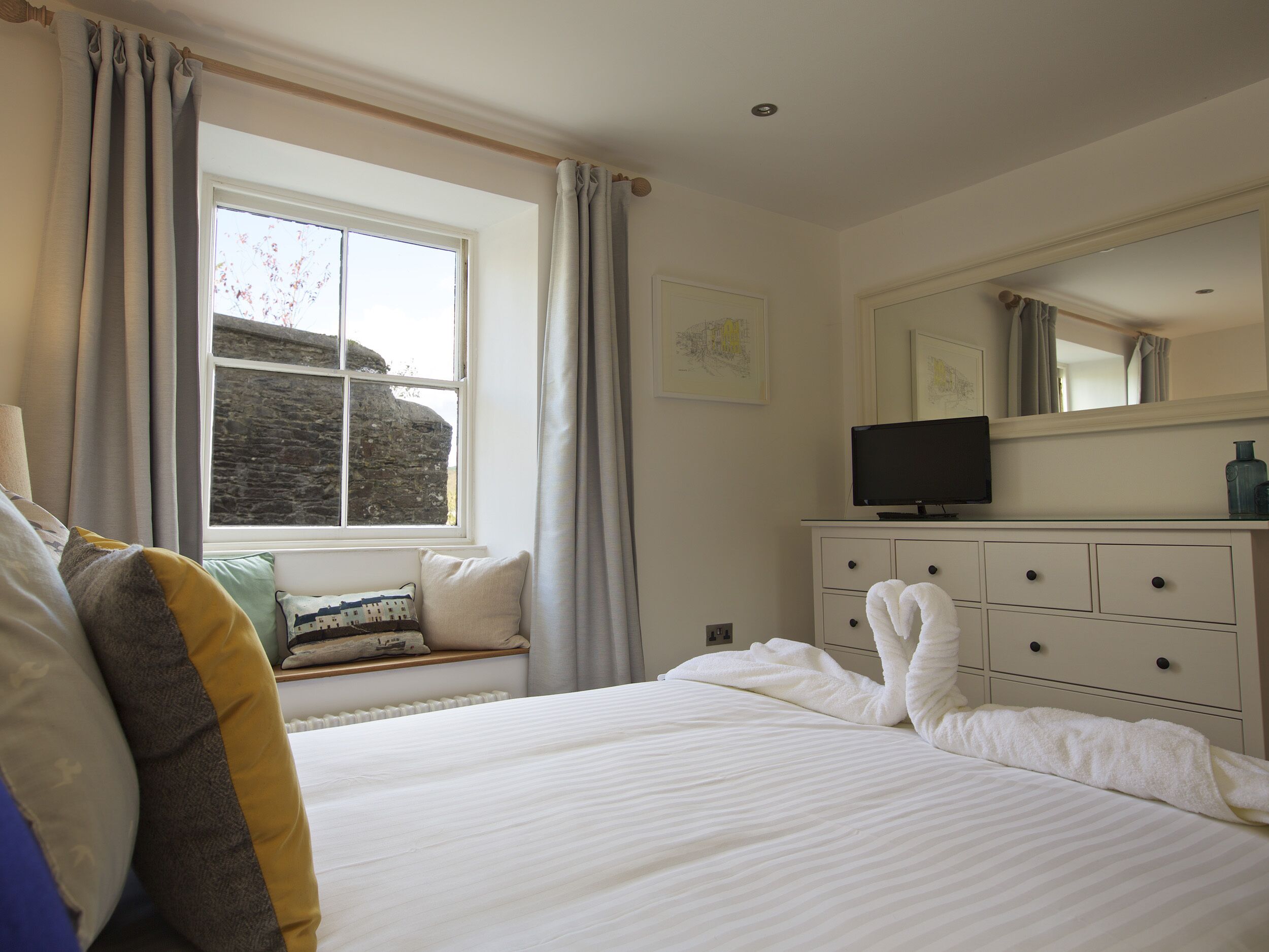 A hotel room with a large bed, a dresser, a television, and a window with curtains.