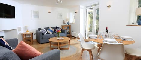 A modern living room with a grey sofa, a coffee table, and a dining area with white chairs and a wooden table.