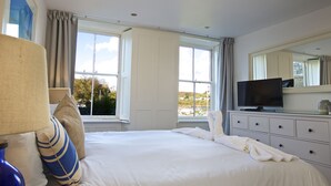 Quarto de hotel com uma cama grande, televisão, penteadeira e janela com vista para o exterior.