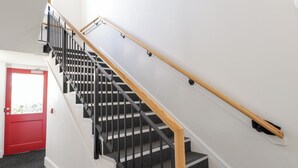 A staircase with black railings and wooden handrails, leading to a landing with a red door. - The Nook (Inverness)