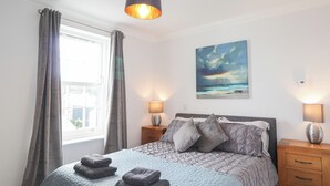 A bedroom with a bed, two bedside tables, a painting, and a window with curtains. - The Nook (Inverness)