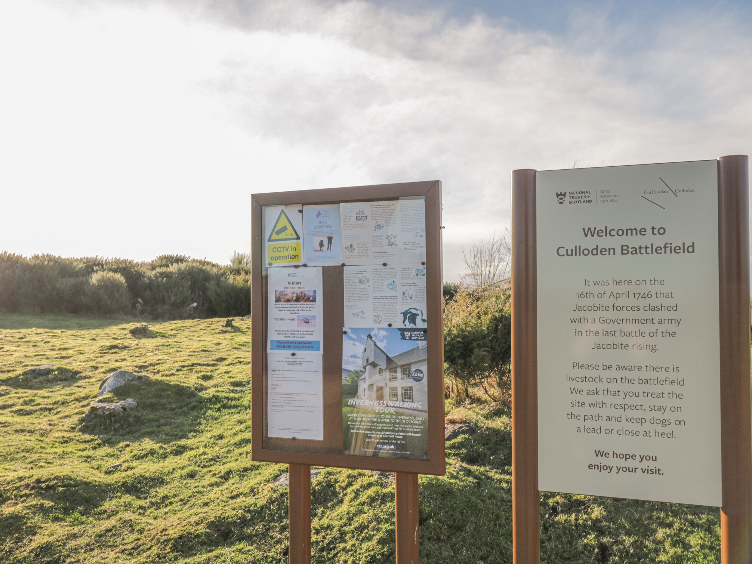 A welcome sign at Culloden Battlefield with informational posters and a CCTV warning sign.