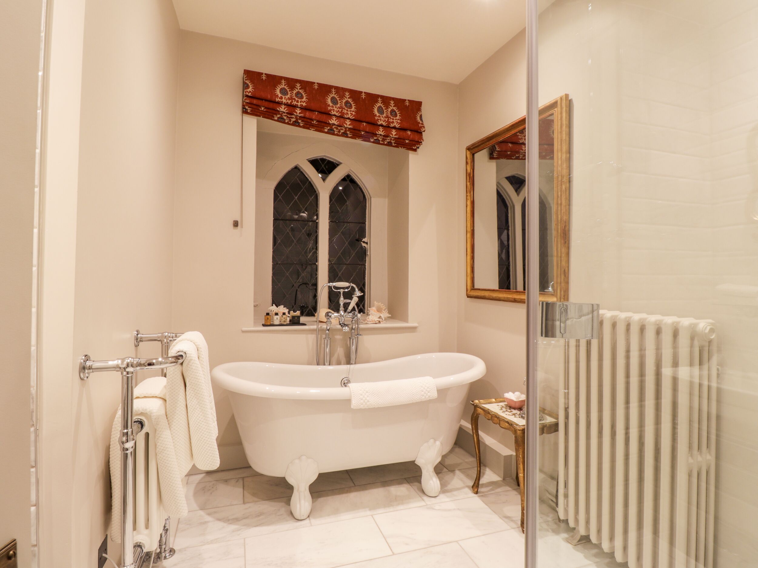 Un baño con bañera independiente, una ventana con un adorno decorativo y un radiador.
