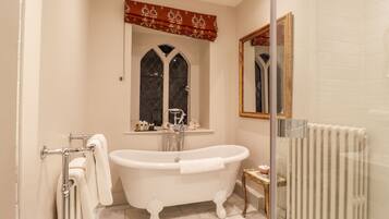Un baño con bañera independiente, una ventana con un adorno decorativo y un radiador.