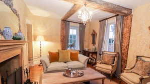 Een gezellige woonkamer met een open haard, een bank, een bijzettafeltje en een kroonluchter.