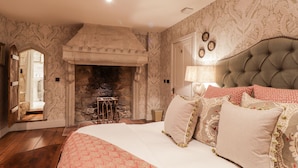 Een slaapkamer met een open haard, een groot bed met veel kussens, en behang met een patroon.