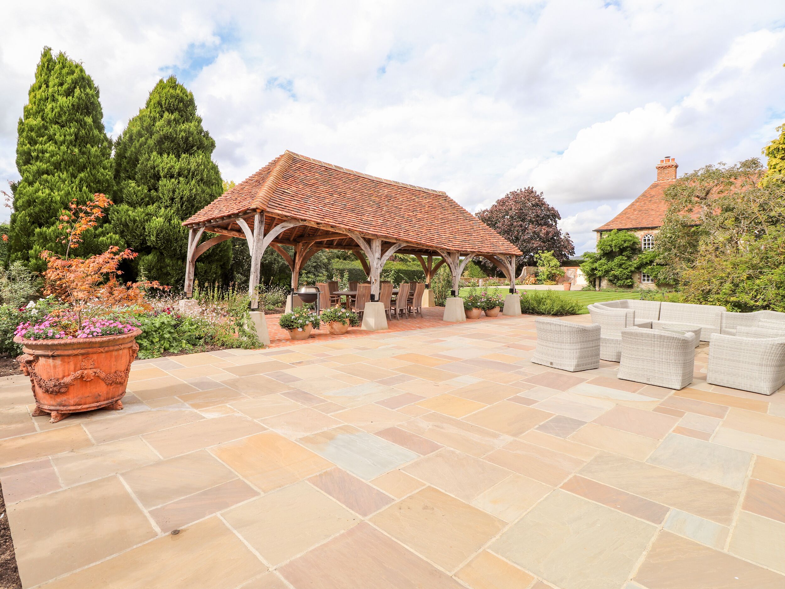 A covered outdoor patio with stone flooring, a wooden pergola, and outdoor furniture.
