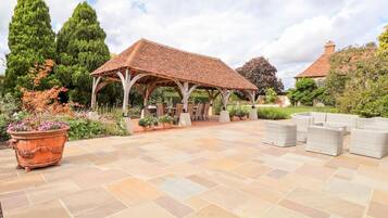 A covered outdoor patio with stone flooring, a wooden pergola, and outdoor furniture.