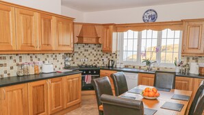 Una cocina con armarios de madera, salpicadero de azulejos, estufa y comedor con mesa y sillas.