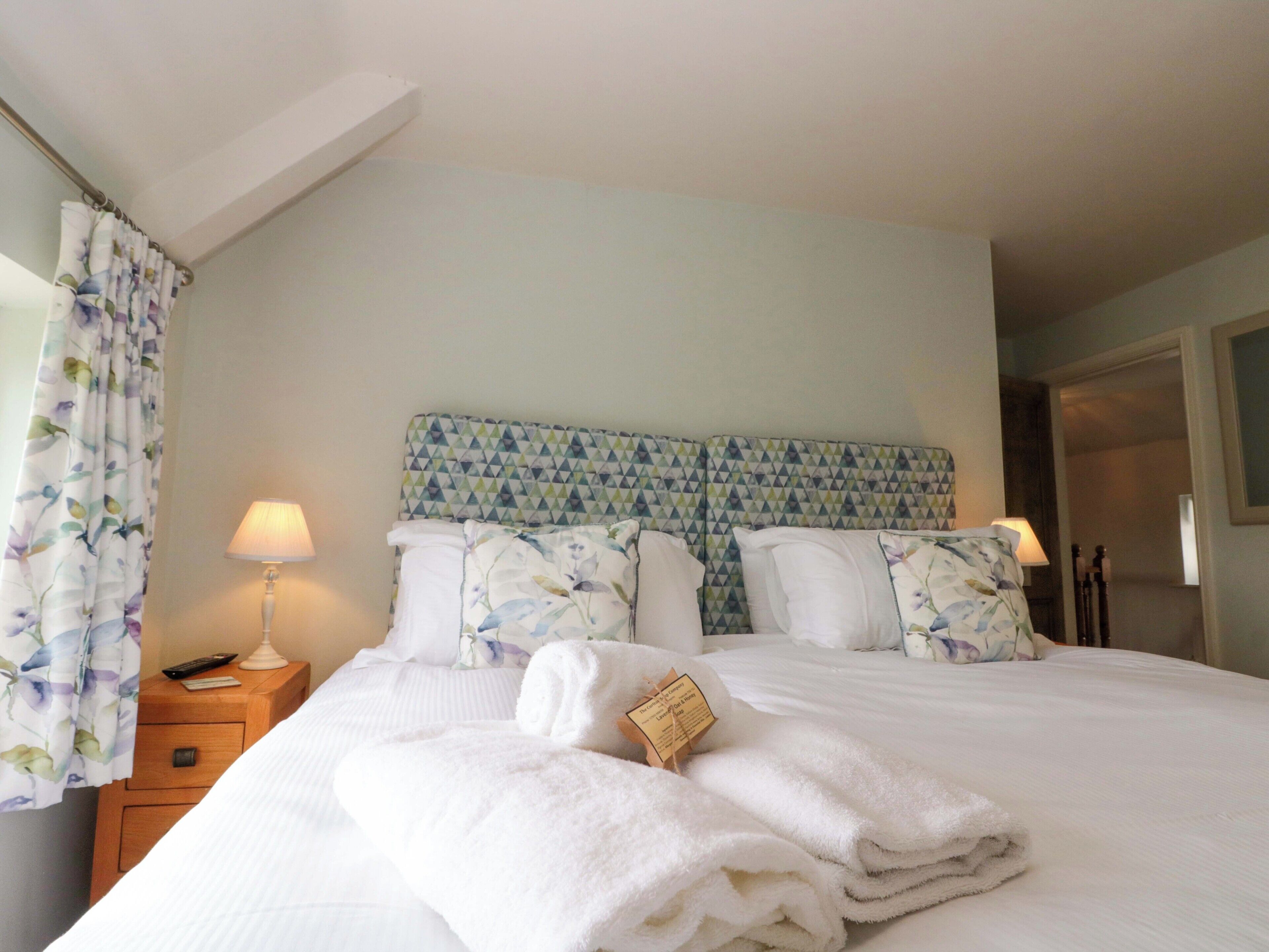A neatly made bed with a patterned headboard, a bedside table with a lamp, and a floral curtain.