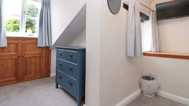 A room with a wooden wardrobe, a blue dresser, a mirror, a television, and a window with curtains. - Weavers Cottage (Middlesbrough)