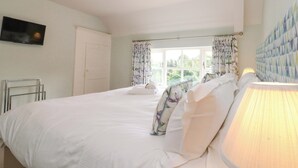 A bedroom with two beds, a television, a window with curtains, and a lamp. - Weavers Cottage (Middlesbrough)