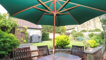 A patio with a wooden table and chairs, a green umbrella, and a stone wall.