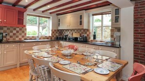 A dining area with a wooden table set for six, surrounded by white chairs. - Weavers Cottage (Middlesbrough)