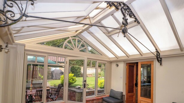 A conservatory with a glass roof, a patio area with seating, and a view of the garden outside. - Weavers Cottage (Middlesbrough)