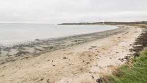 Une plage de sable avec une côte incurvée, un bâtiment visible au loin et un ciel nuageux.