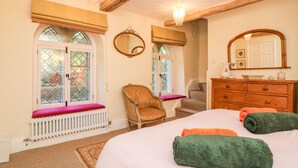 Ein Schlafzimmer mit einem Bett, zwei Fenstern mit Fensterläden, einem Sessel, einem Schminktisch und einem Spiegel.