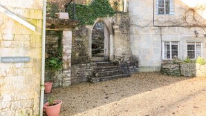 Ein Steinhaus mit einem Schild, auf dem 'CHAPEL COTTAGE' steht, einem Kiesweg und einem kleinen Gartenbereich mit Topfpflanzen.