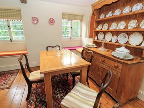 A dining area with a wooden table, chairs, a bench, and a cabinet with plates. - Chapel Cottage (Stroud)