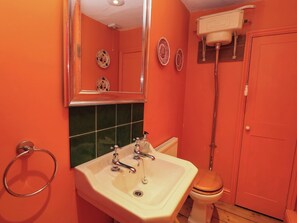 A bathroom with a white sink, two faucets, a mirror, and a toilet. - Chapel Cottage (Stroud)