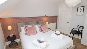 A bedroom with a large bed, two bedside lamps, a fluffy rug, and a white door. - Cambrie (Tenby)