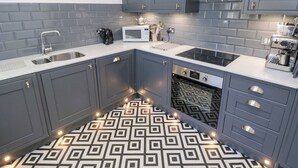 A modern kitchen with grey cabinets, a white countertop, a built-in oven, a microwave, and a clock on the wall. - Cambrie (Tenby)