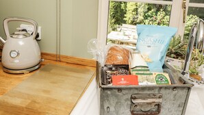 A kitchenette with a kettle, a bread loaf, a bag of crisps, a chocolate bar, and a milk carton. - Corner Cottage (Carnforth)