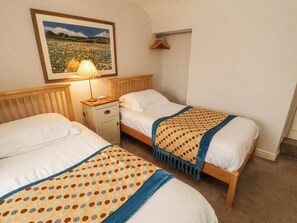Quarto com duas camas, uma mesinha de cabeceira, abajur, quadro na parede e cabide de madeira.