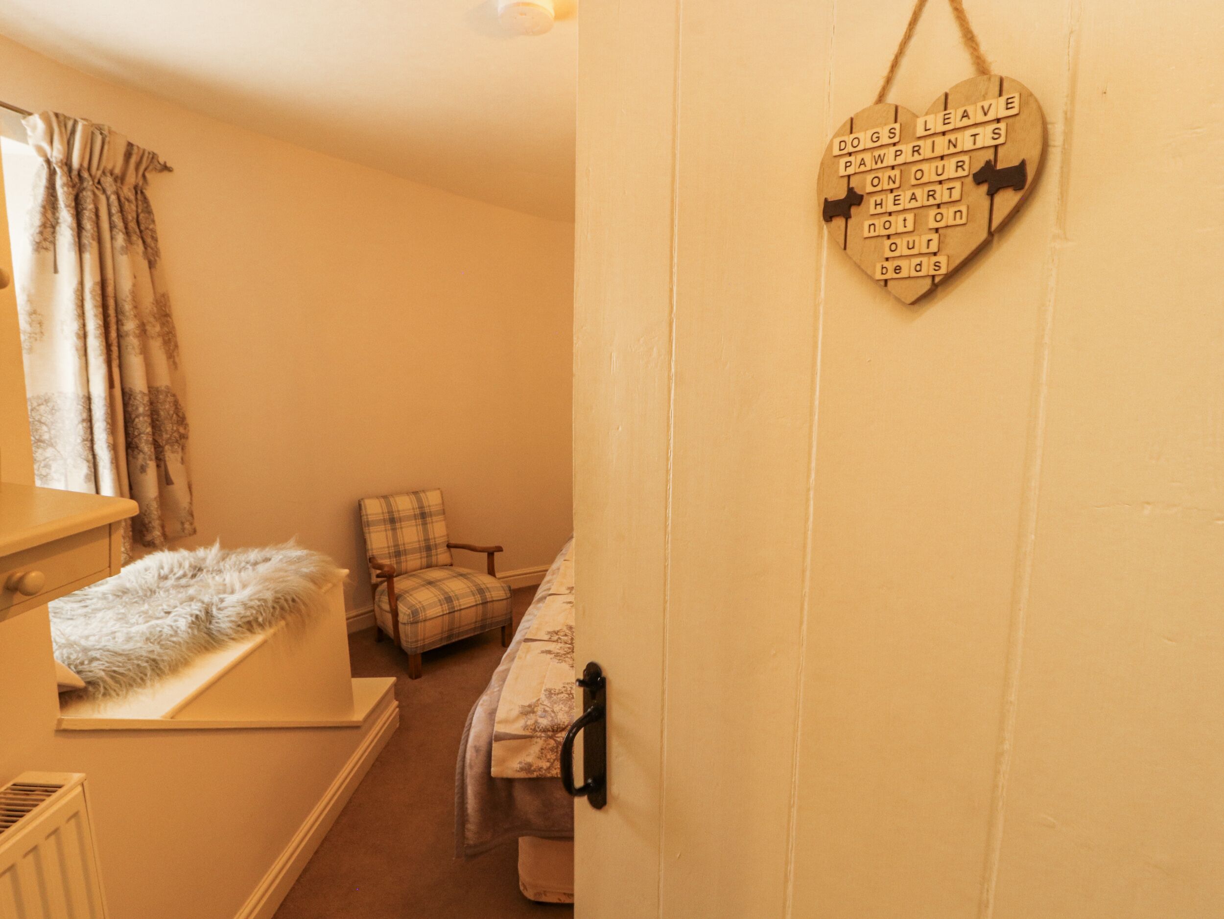 A cozy room with a plaid armchair, a fluffy white rug, and a heart-shaped sign on the wall.