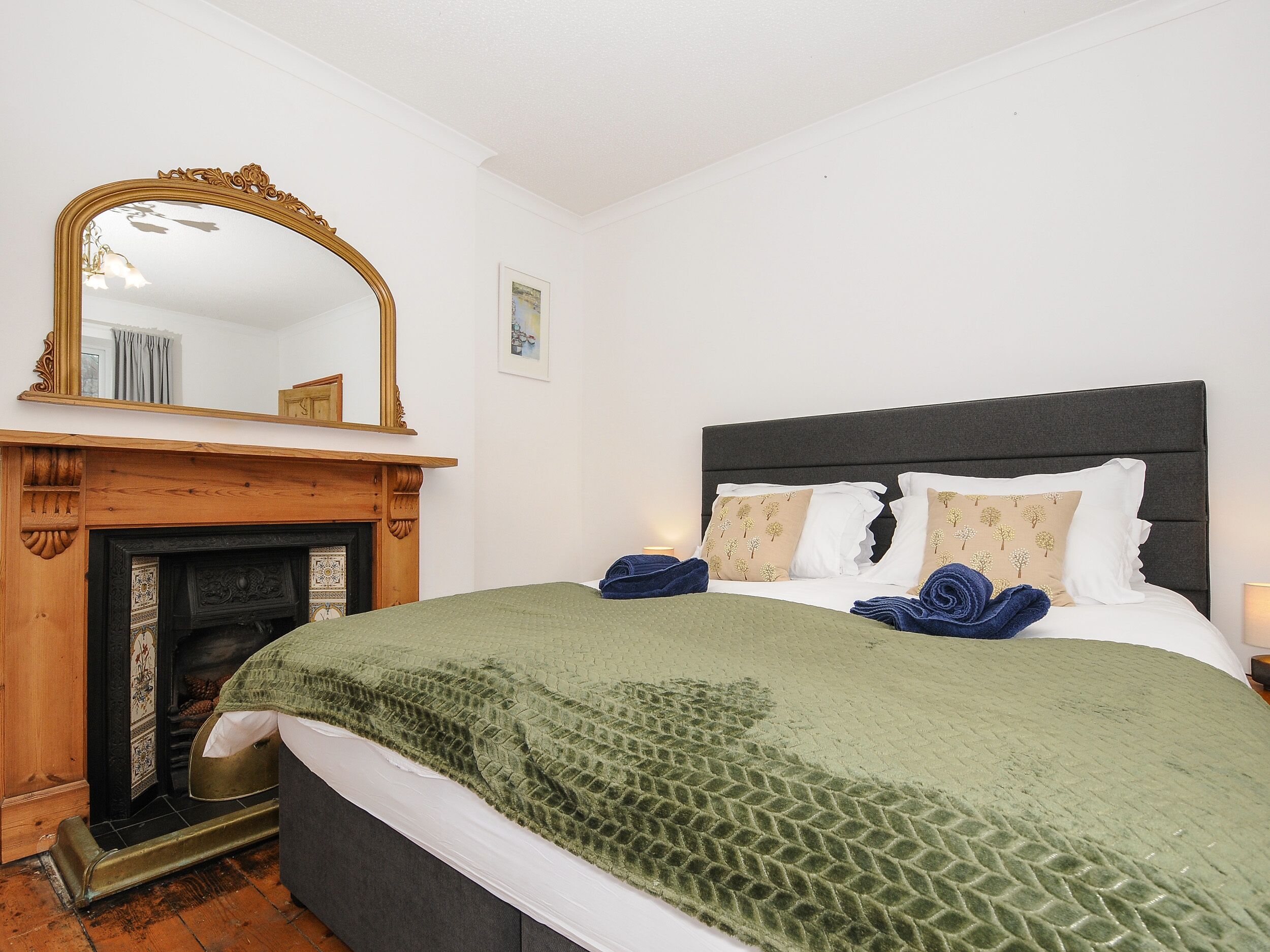 A bedroom with a bed, a fireplace, a mirror, and a nightstand.