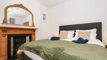 A bedroom with a bed, a fireplace, a mirror, and a nightstand.