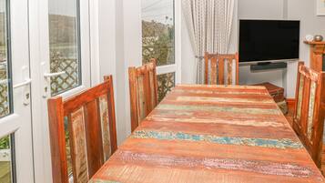 Un área de comedor con una larga mesa de madera y sillas, un televisor y vistas al exterior.